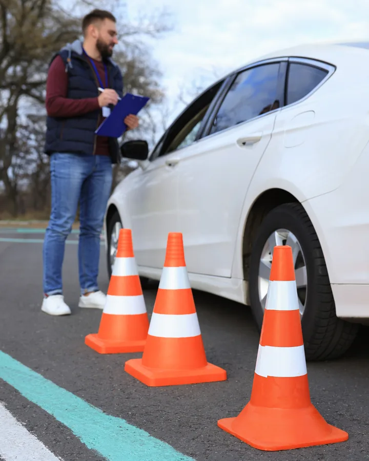 Instruktor sa čeklistom pored automobila i saobraćajnih čunjeva na poligonu auto-škole